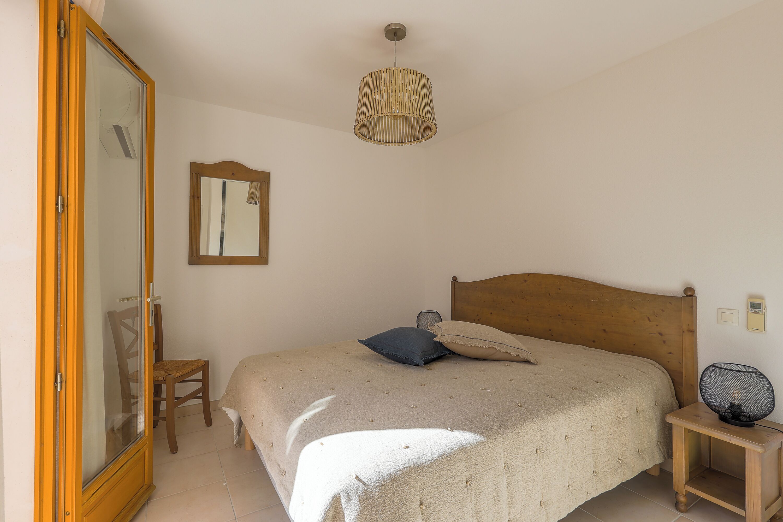 A bedroom with a bed, a wooden headboard, a bedside table with a lamp, a mirror, and a wardrobe.