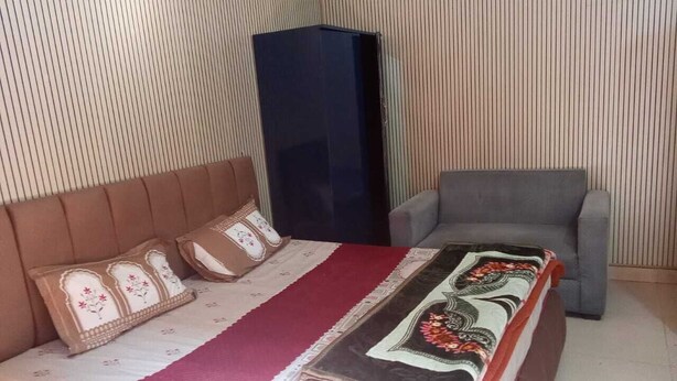 A bedroom with a bed, a grey armchair, and a dark-colored wardrobe. - Hotel Ganga vardan (Rishikesh)