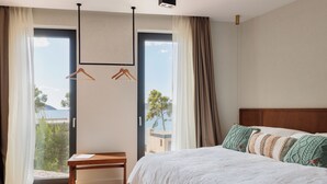 A bedroom with a bed, a wooden table, and a view of the outdoors through a large window. - Pine View Bay, Hvar Island (Stari Grad)