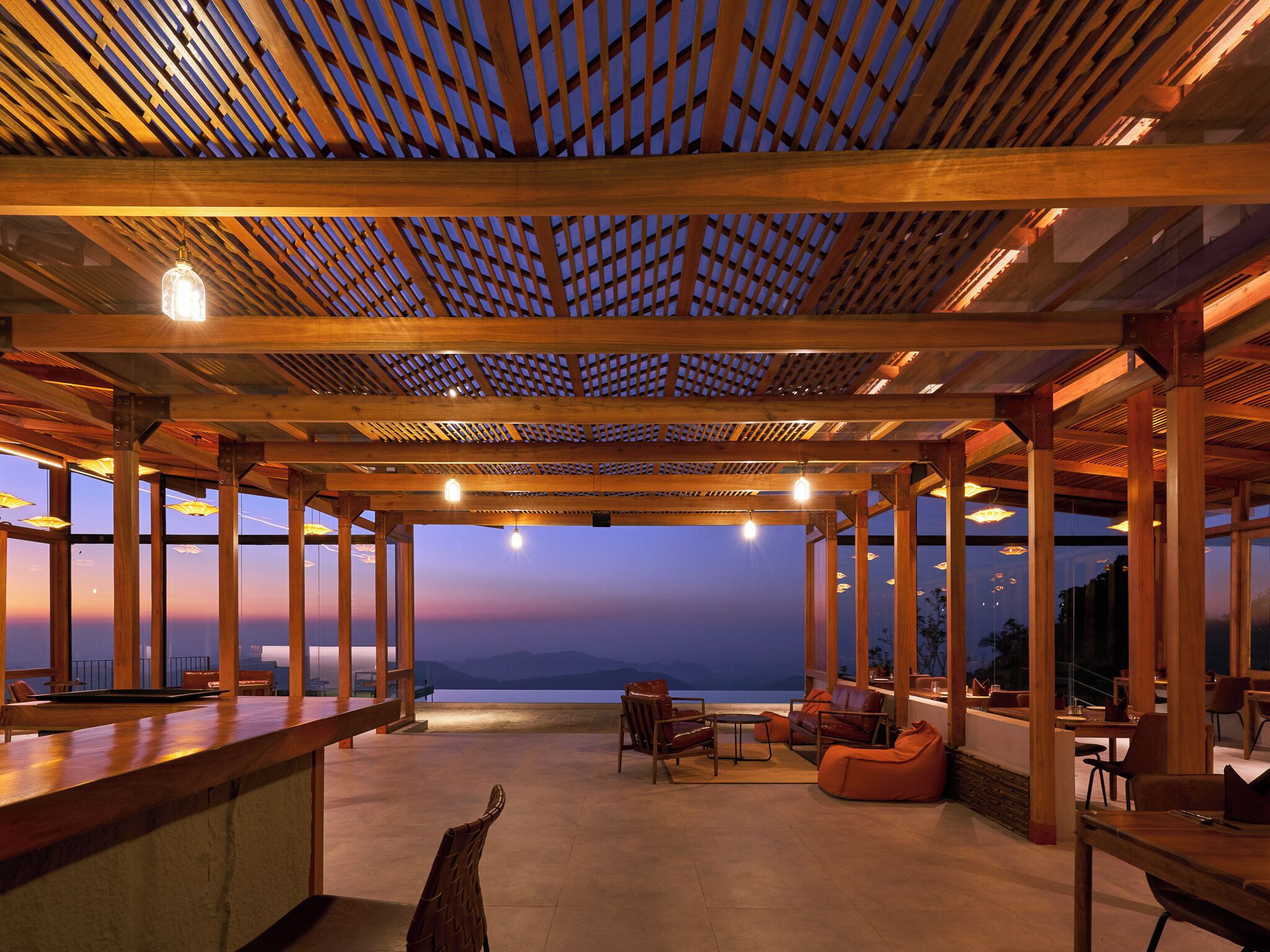 An open-air terrace with wooden beams and large windows overlooking a scenic view.