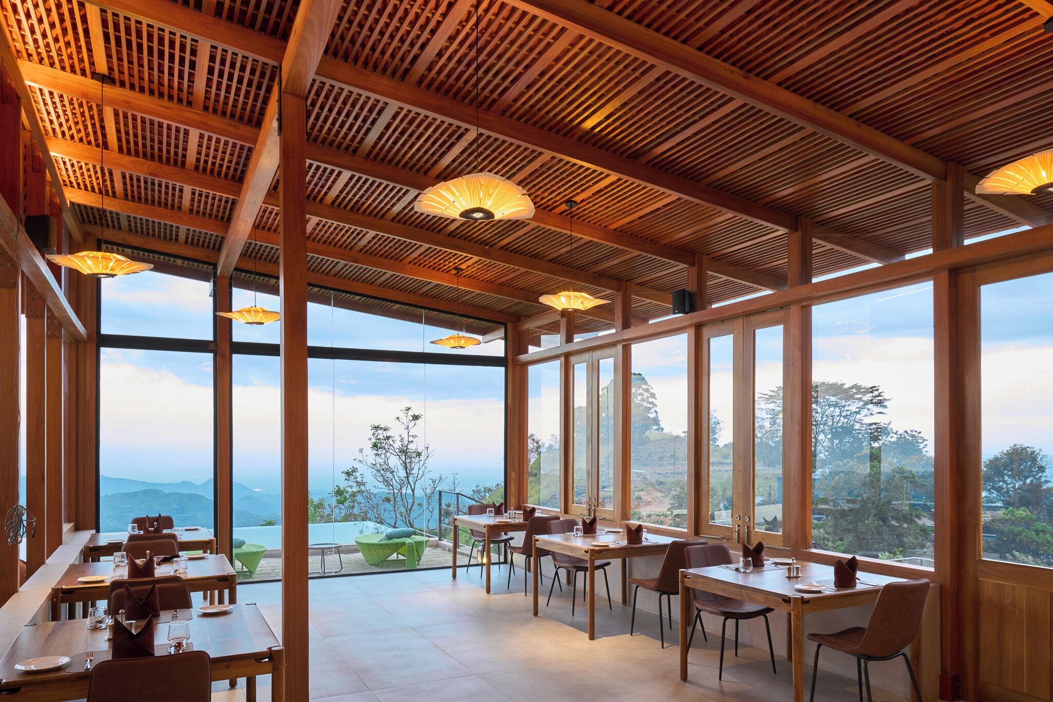 A restaurant with wooden beams and large windows offering a view of the mountains. Tables are set with chairs and dining ware.