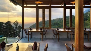 A restaurant with large windows offering a view of the hills. Tables are set with chairs and table settings. - Wishing Tree Boutique Resort Haputale (Haputale)