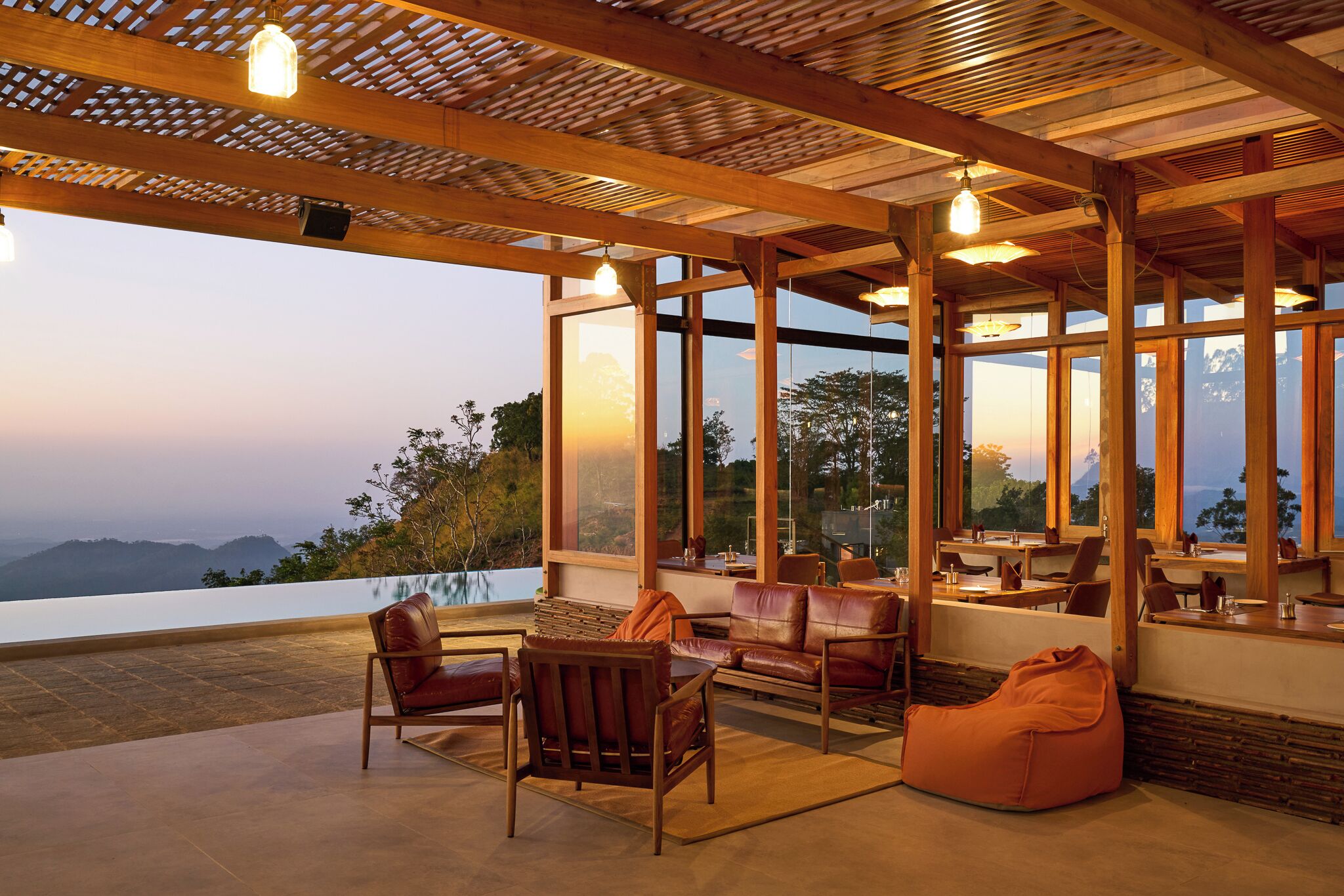 A spacious outdoor seating area with wooden furniture and large windows offering a view of the mountains.
