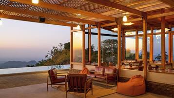 A spacious outdoor seating area with wooden furniture and large windows offering a view of the mountains.
