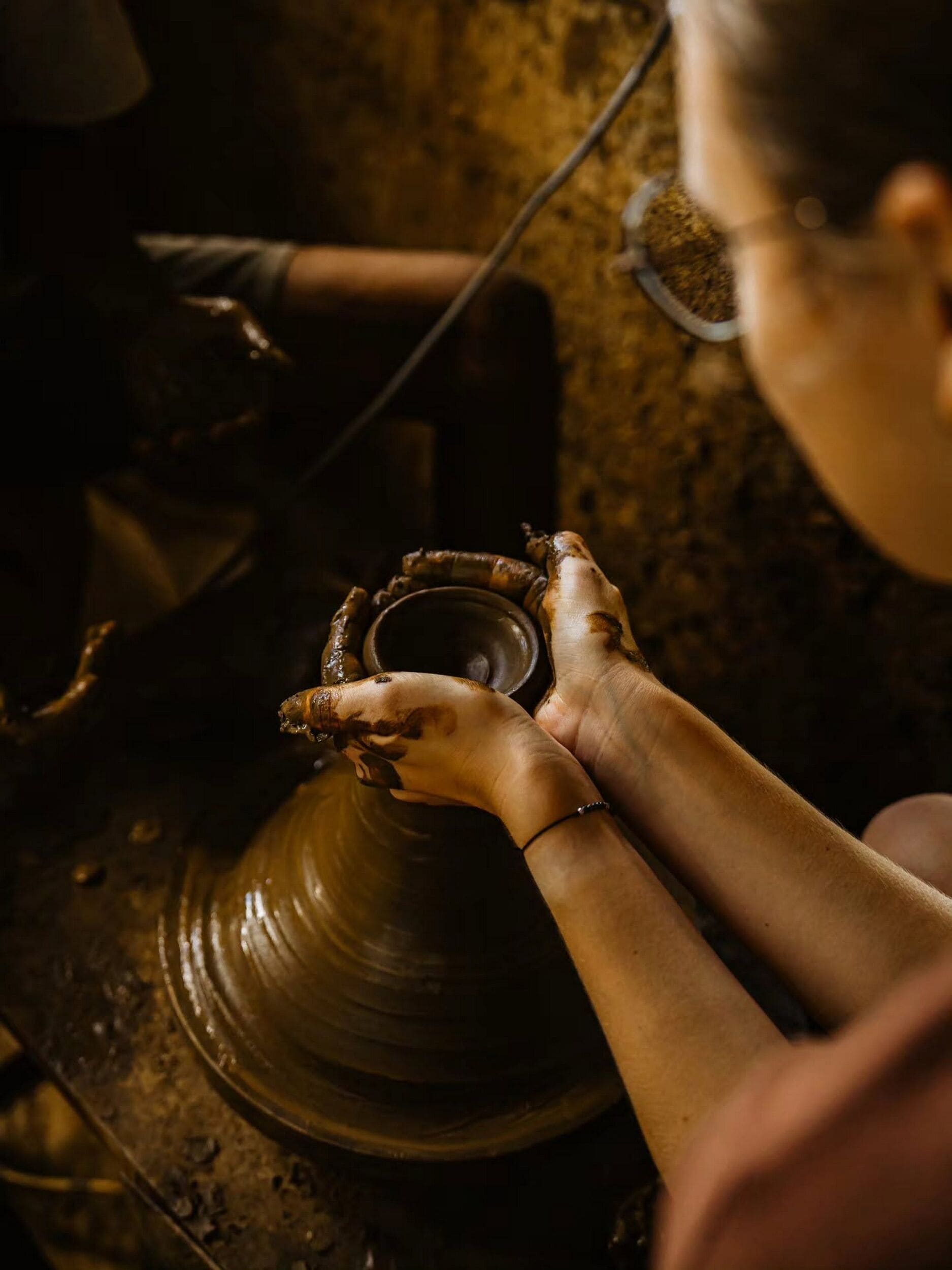 A person shaping a clay pot on a pottery wheel.