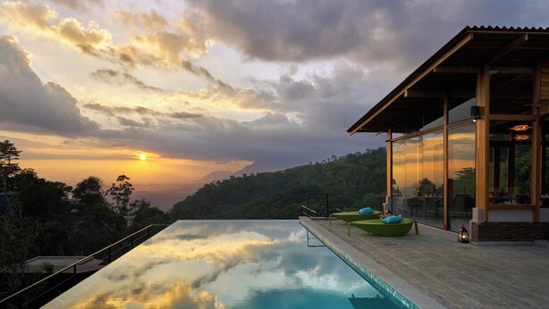 An infinity pool with a view of a sunset and mountains. There are lounge chairs and a building with large windows. - Wishing Tree Boutique Resort Haputale (Haputale)