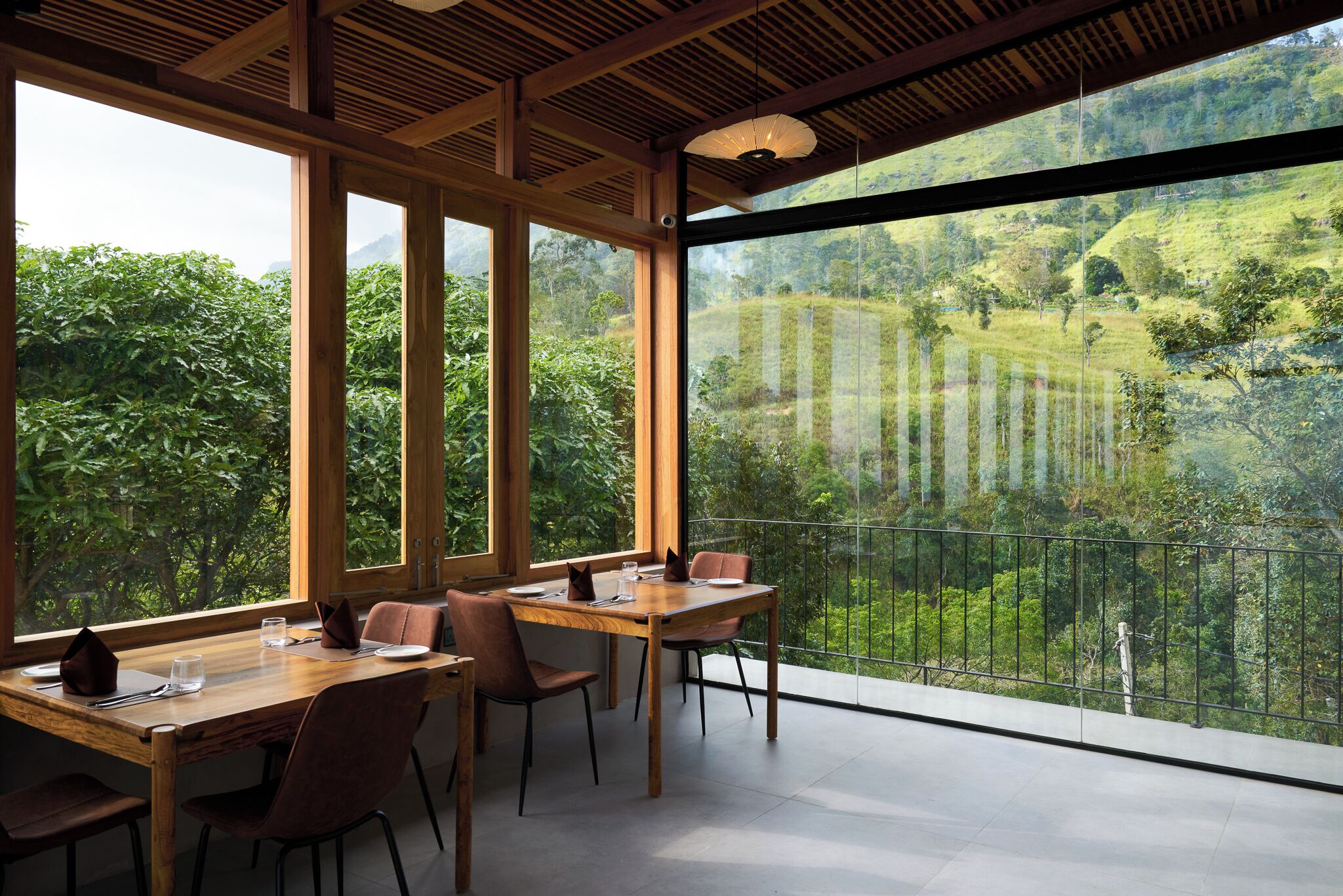 A dining area with a large table and chairs, large windows with a view of a lush green landscape.
