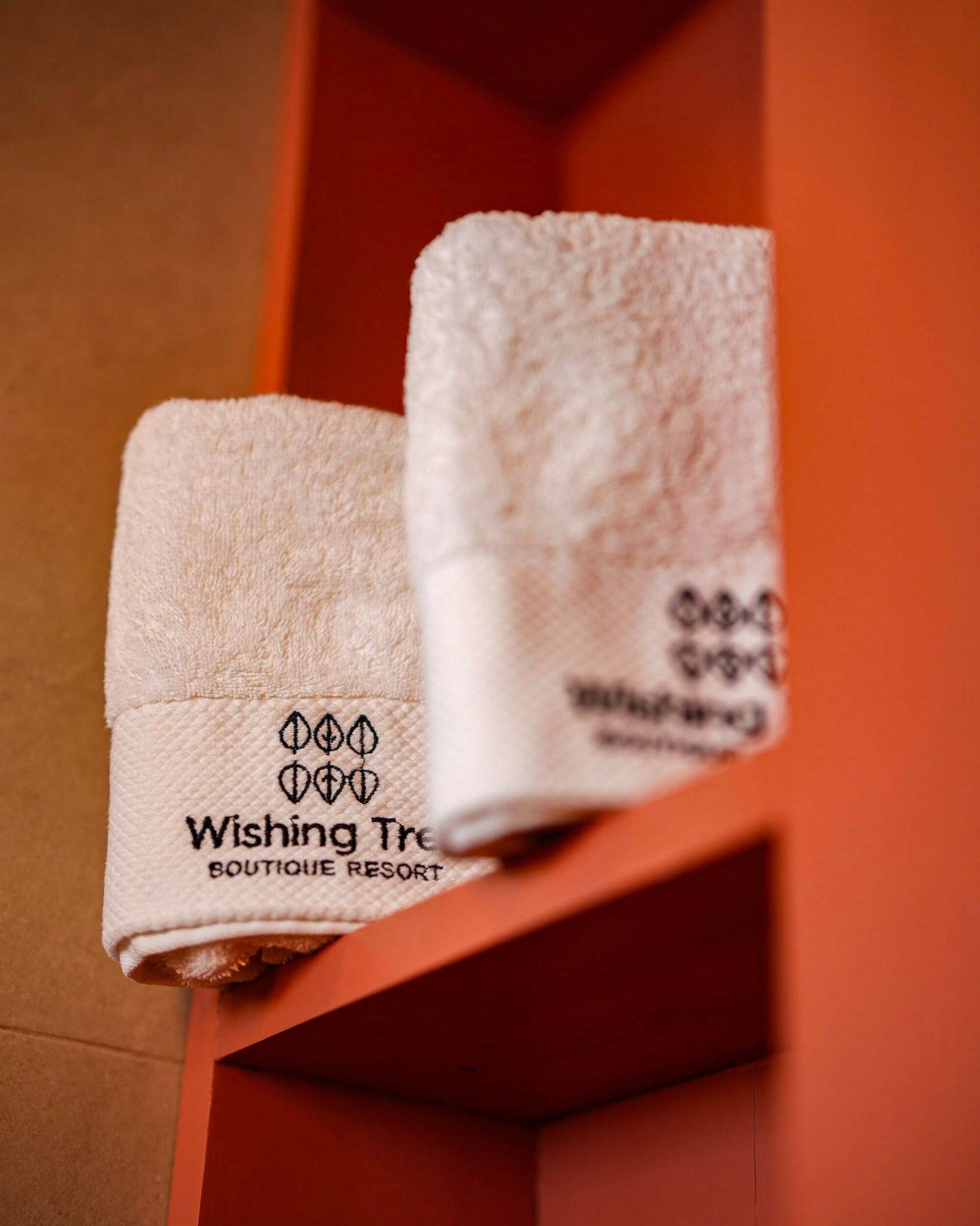 Two folded towels with 'Wishing Tree Boutique Resort' branding on a shelf.