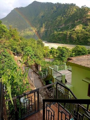Vista desde un balcón con vista a un río, con un arcoíris en la distancia y abundante vegetación.