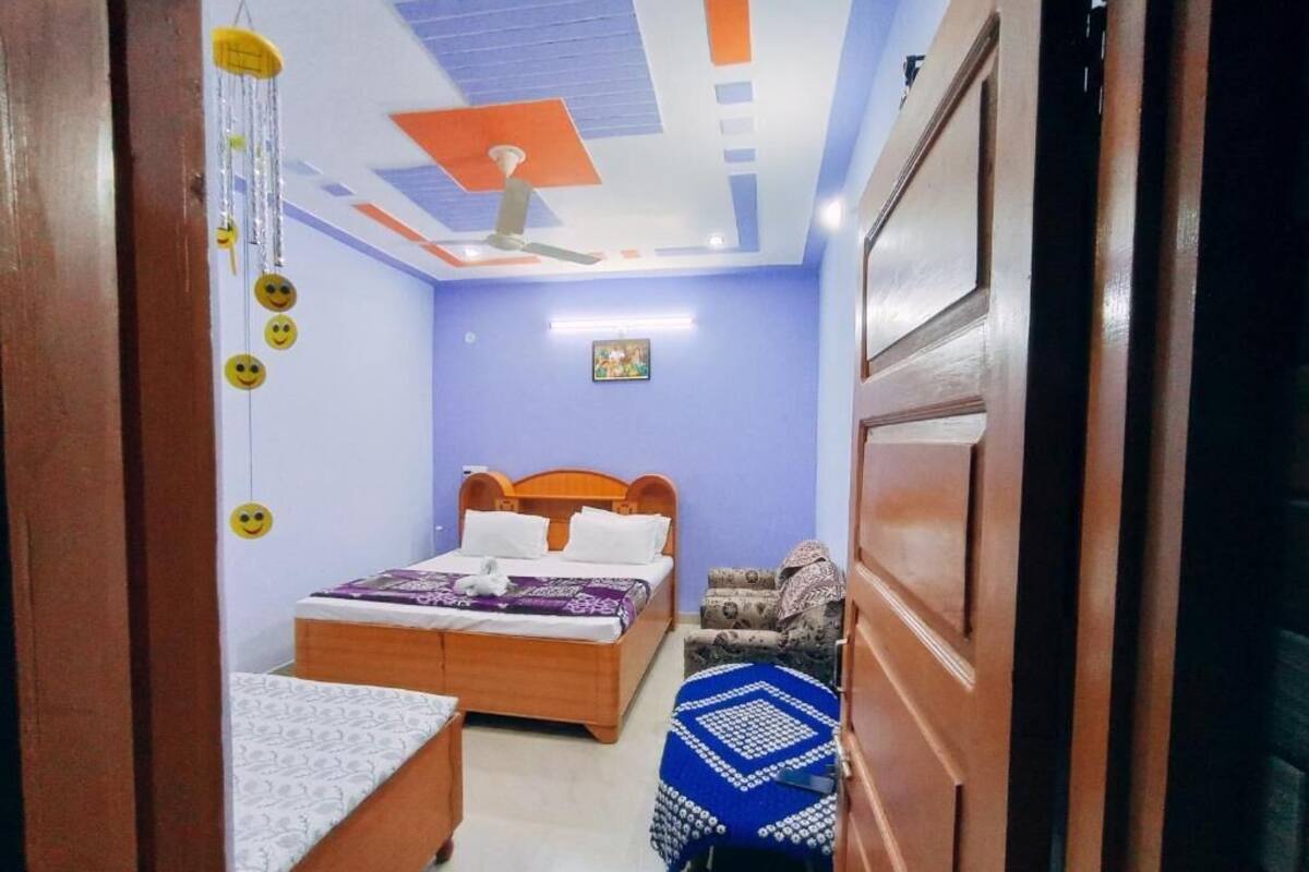 Un dormitorio con una cama, una silla, una mesita de noche, un ventilador de techo y un cuadro colgado en la pared.