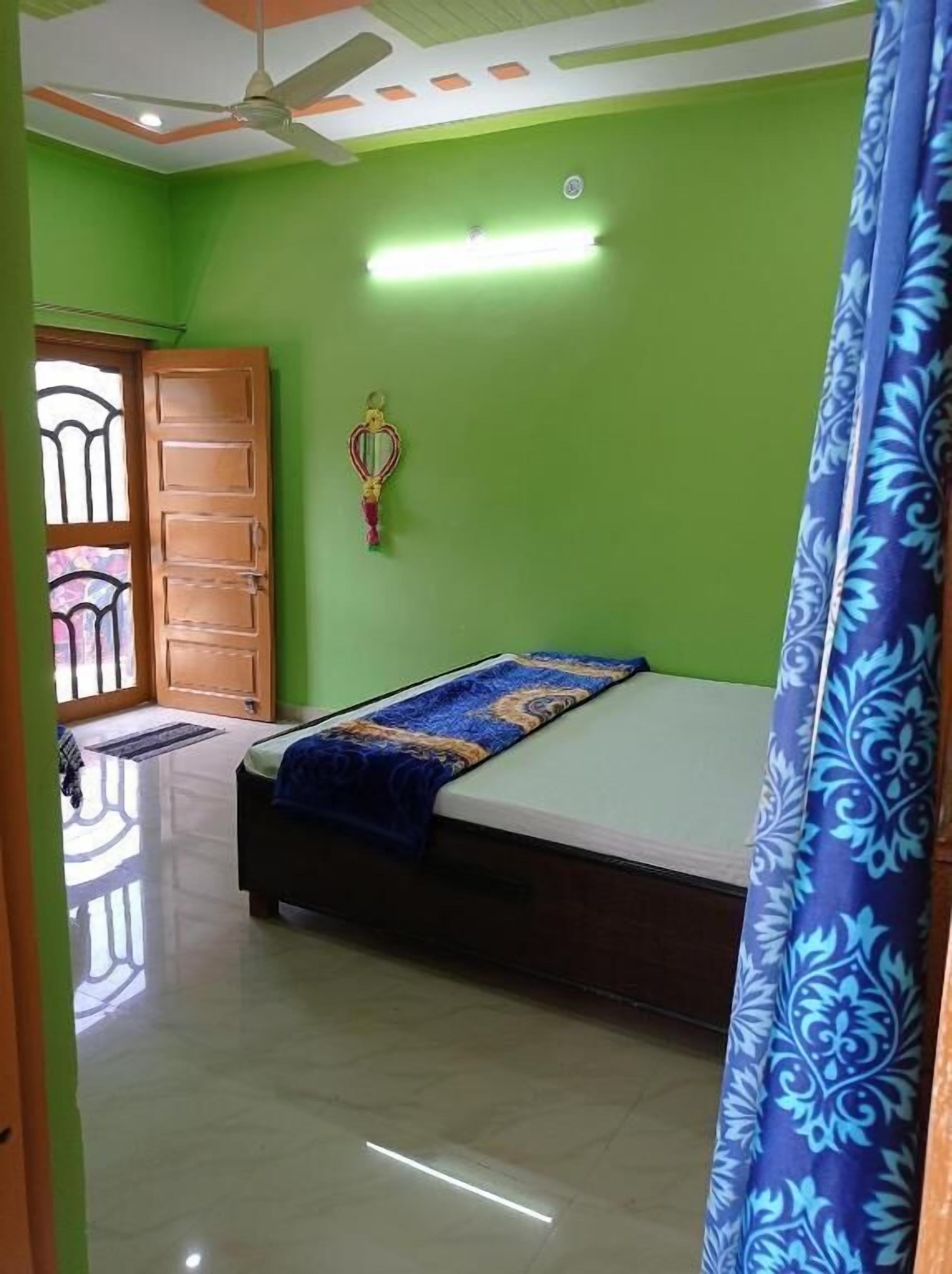 A bedroom with a bed, a ceiling fan, a green wall, and a window with a metal gate.