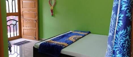 Ein Schlafzimmer mit einem Bett, einem Deckenventilator, einer grünen Wand und einem Fenster mit einem Metallgitter.