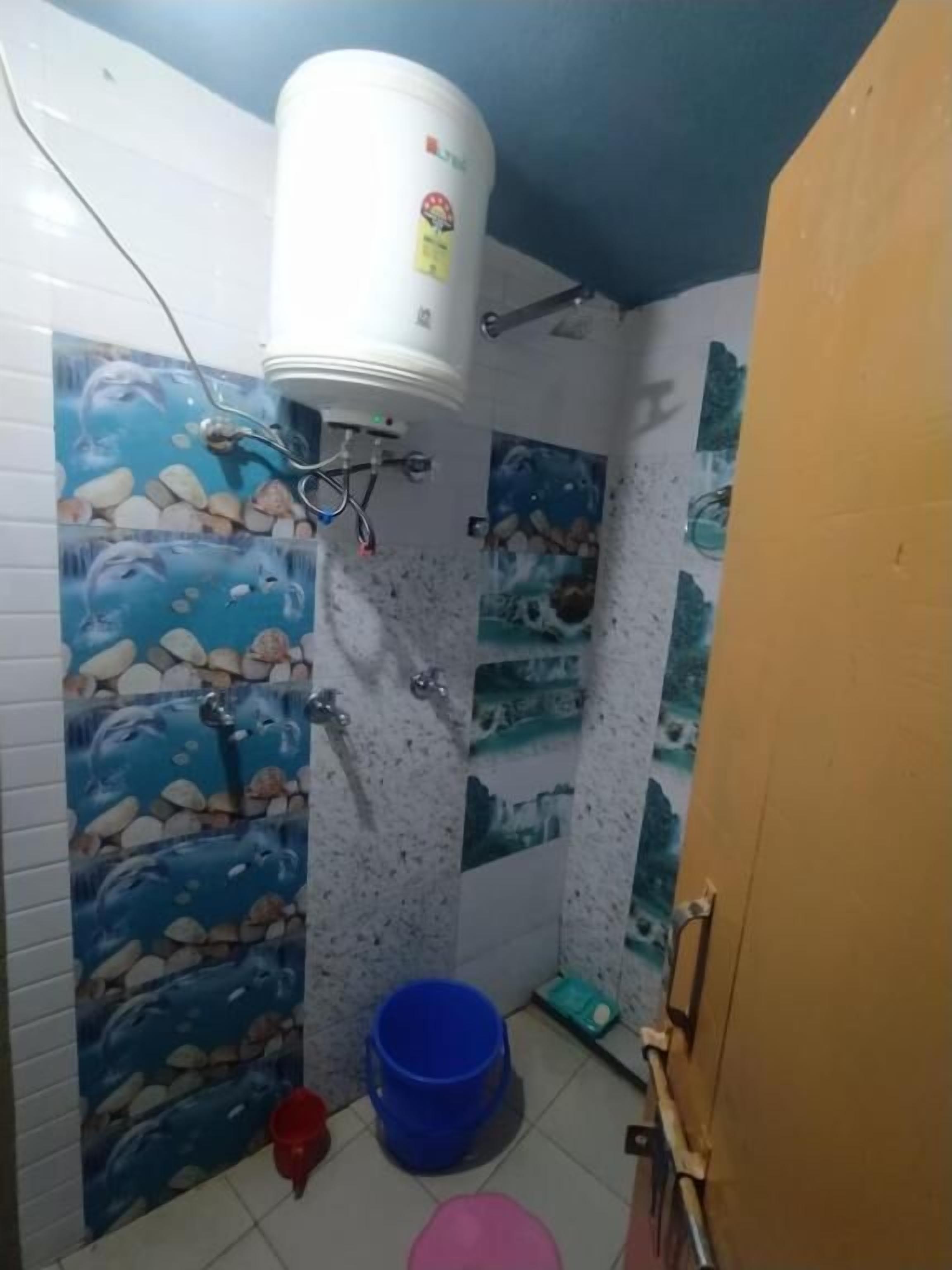 A bathroom with a white water heater, a blue bucket, and a red bucket on the floor.