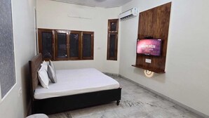 A bedroom with a bed, a TV mounted on the wall, and a window with wooden frames.