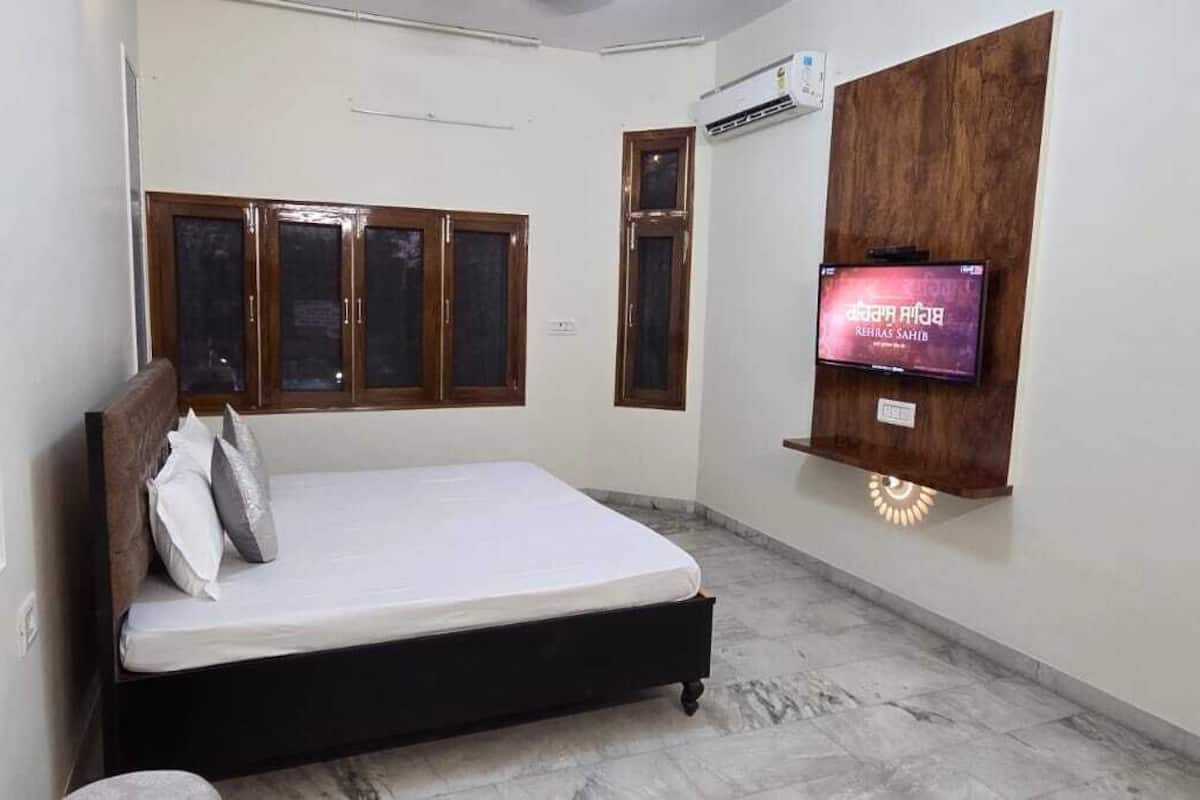 A bedroom with a bed, a TV mounted on the wall, and a window with wooden frames.