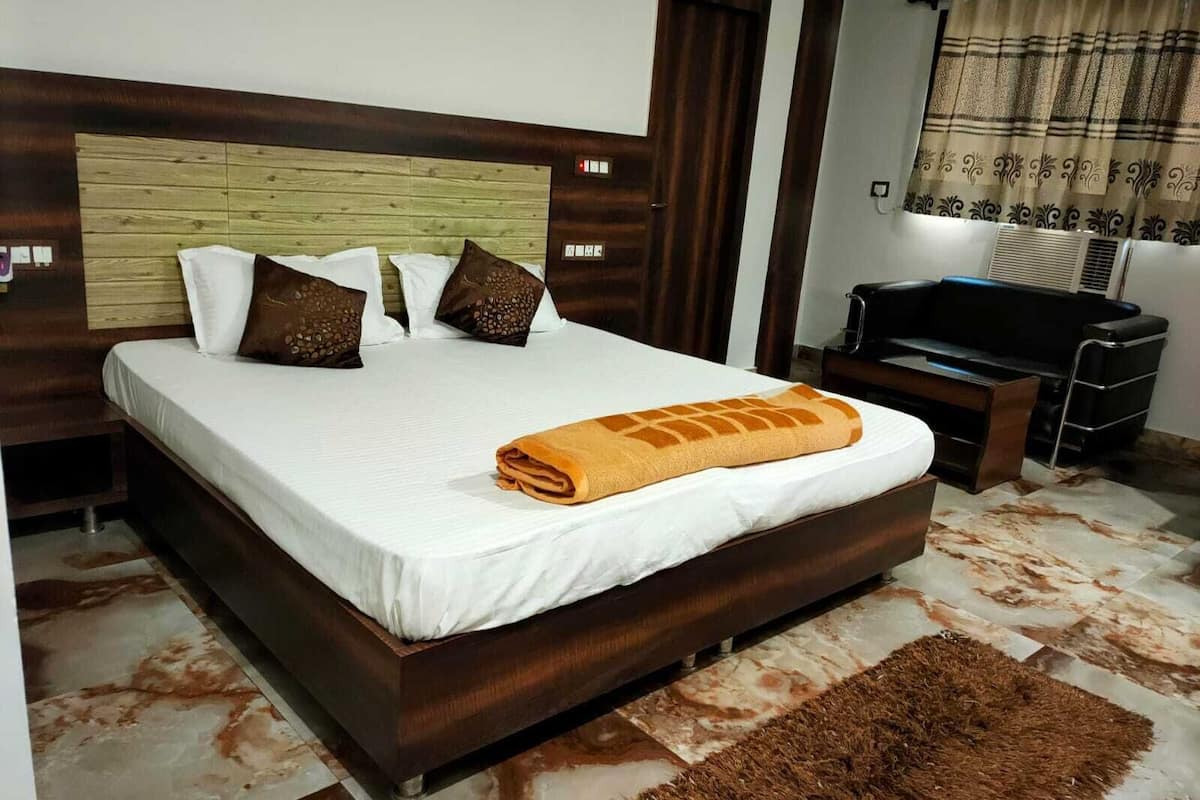A bedroom with a wooden headboard, a bed with white bedding, brown pillows, a brown rug, and a black TV stand with a remote control.