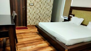 A hotel room with a wooden floor, a bed with white linens, a desk, and a wall with a patterned design.
