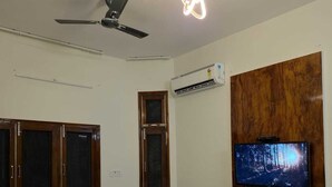 A bedroom with a bed, a ceiling fan, an air conditioning unit, and a mounted TV.