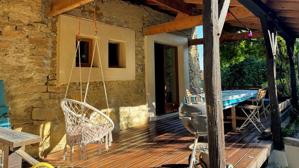 Une terrasse extérieure rustique avec une table en bois, un fauteuil suspendu et un barbecue.