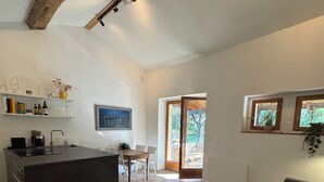 Une cuisine moderne avec un îlot central, un coin repas avec une table et des chaises, un canapé gris et une petite table ronde sur laquelle est posé un magazine.