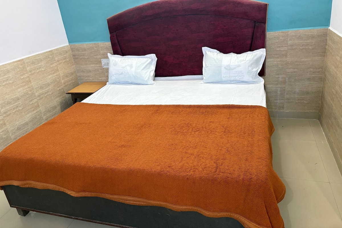 Una cama bien tendida con una manta marrón, almohadas blancas y un cabecero oscuro en una habitación con paredes azules y beige.