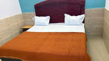 Una cama bien tendida con una manta marrón, almohadas blancas y un cabecero oscuro en una habitación con paredes azules y beige.