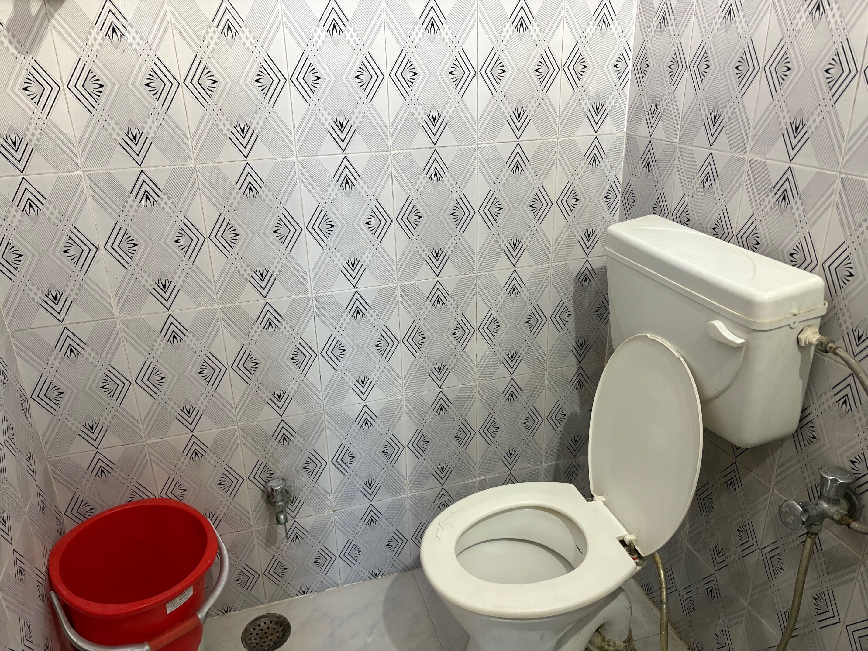 Ein Badezimmer mit Toilette, einem roten Eimer und fliesenmuster.
