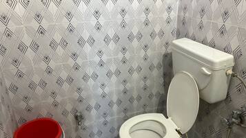 Ein Badezimmer mit Toilette, einem roten Eimer und fliesenmuster.