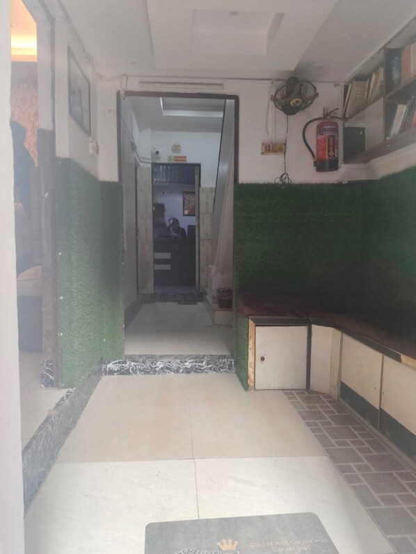 Un couloir avec un tapis, un extincteur et un ventilateur fixé au mur.
