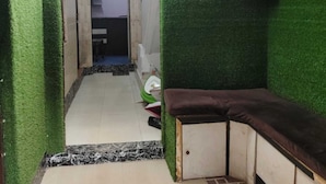 Un couloir étroit aux murs recouverts de gazon synthétique vert, avec un banc et un ventilateur sur le côté droit.