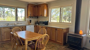 A kitchen with wooden cabinets, a dining table with chairs, a microwave, and a wood-burning stove. - Spacious and private country estate (Whiteheads Creek)