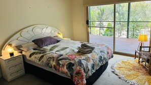 A bedroom with a bed, bedside lamps, a ceiling fan, a window with a view of greenery, and a chair with a lamp. - Spacious and private country estate (Whiteheads Creek)