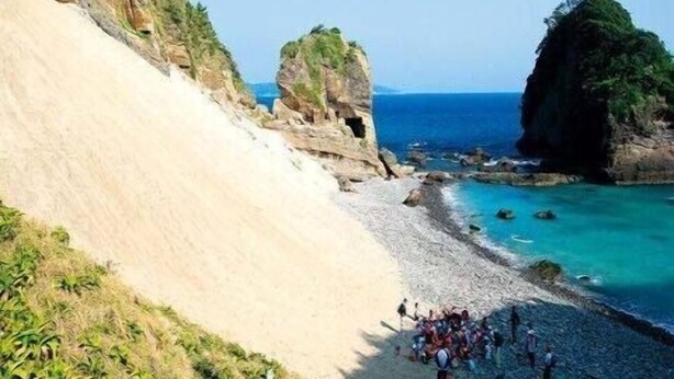 A coastal area with a rocky beach, a cliff, and a group of people gathered near the water. - Minami Izu Yumigahama Onsen Kominka no Yado Sankai (Minamiizu)