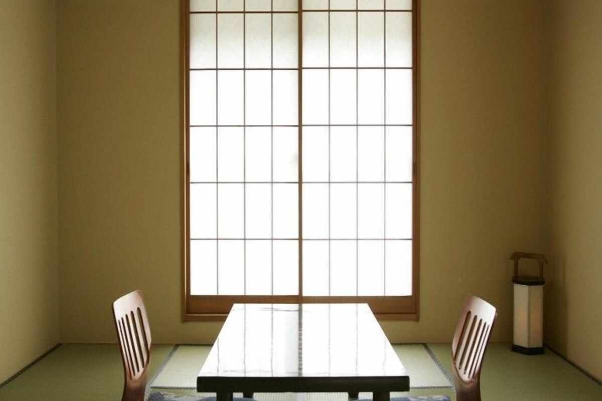 A traditional Japanese room with tatami flooring, a low table, two wooden chairs, and a shoji screen door.