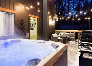 Un bain à remous doté d’une terrasse en bois et d’un espace salon extérieur, le tout agrémenté de guirlandes lumineuses.
