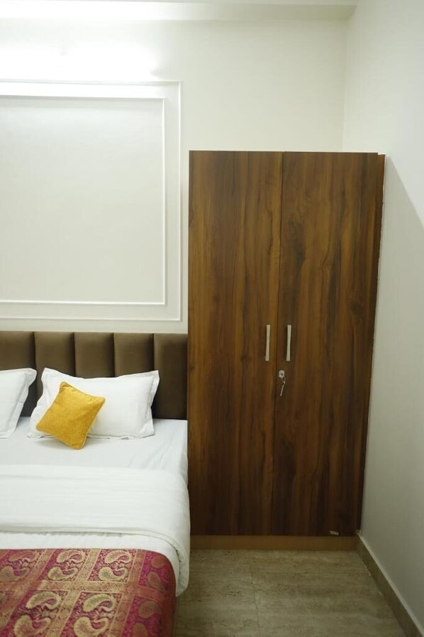 A bedroom with a bed, a wooden wardrobe, and a patterned bedspread. - Bhawani Homes (Varanasi)