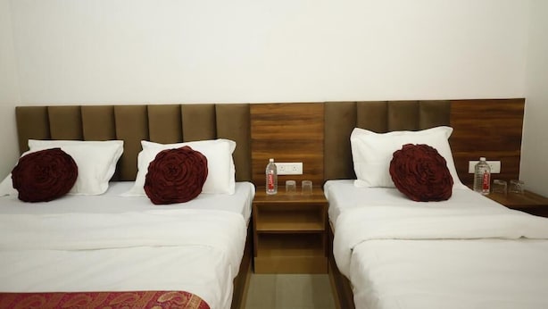 Quarto de hotel com duas camas, cada uma com roupa de cama branca e almofadas decorativas de rosa. Há mesas de cabeceira de madeira com uma garrafa de água e copos.