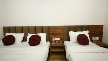 Habitación de hotel con dos camas, cada una con ropa blanca y almohadas decorativas con forma de rosa. Hay mesitas de noche de madera con una botella de agua y vasos.