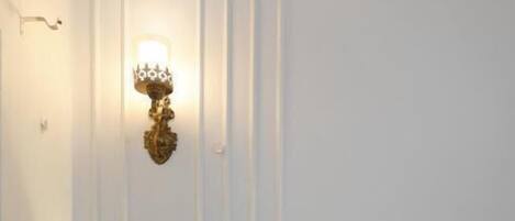 A hotel room with a bed, a nightstand, a wall-mounted light fixture, and a plain wall.