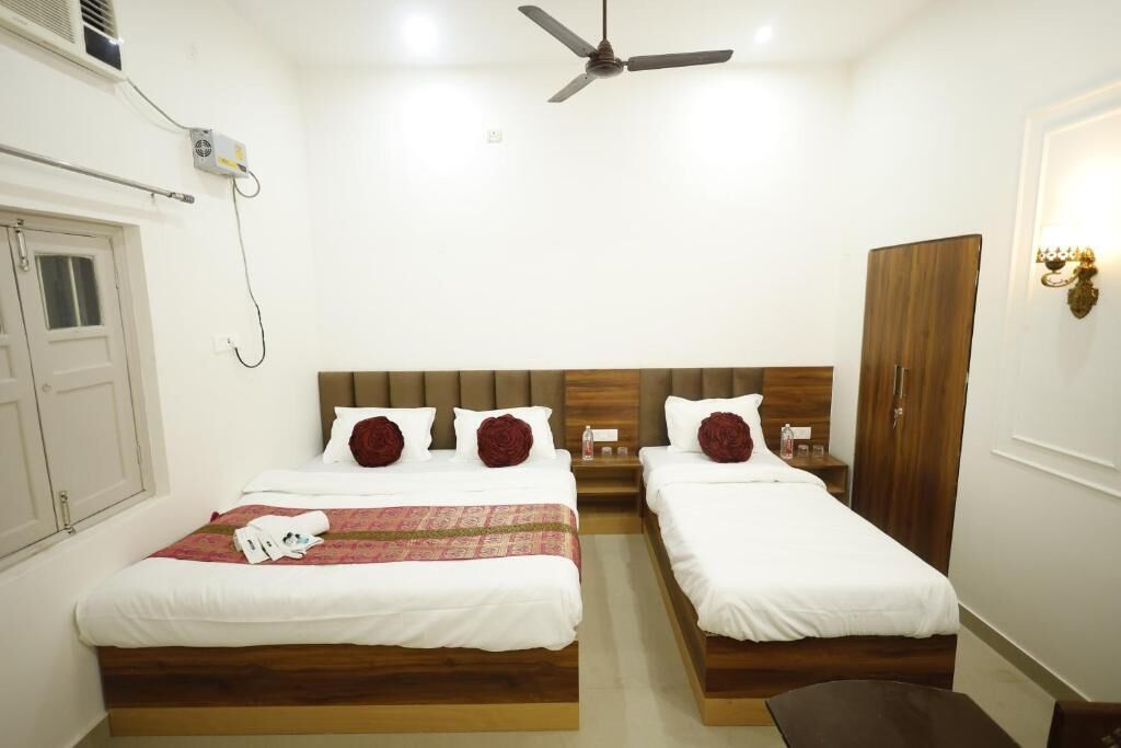 A hotel room with two beds, a ceiling fan, a wardrobe, and a bedside table with a lamp.