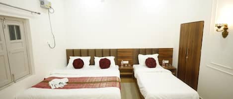 A hotel room with two beds, a ceiling fan, a wardrobe, and a bedside table with a lamp.