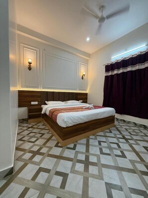 A bedroom with a bed, nightstands, a ceiling fan, and patterned flooring. - Bhawani Homes (Varanasi)
