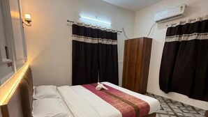 Quarto de hotel com cama, cabeceira de madeira, ventoinha de teto e ar condicionado.