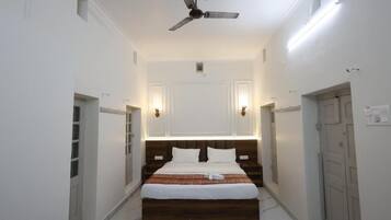 Quarto de hotel com cama, ventilador de teto, arandelas na parede e uma porta.