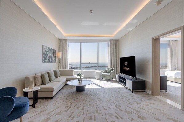 A modern hotel room with a sofa, coffee table, TV, and a view of the city. - Luxury 1BR on Palm Jumeirah | Pool Access & Beach (دبي)