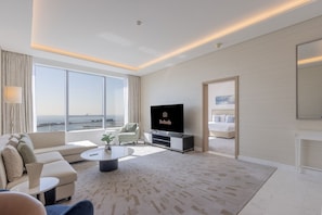 A modern hotel room with a large window, a flat-screen TV, a sofa, a coffee table, and a bed. - Luxury 1BR on Palm Jumeirah | Pool Access & Beach (دبي)