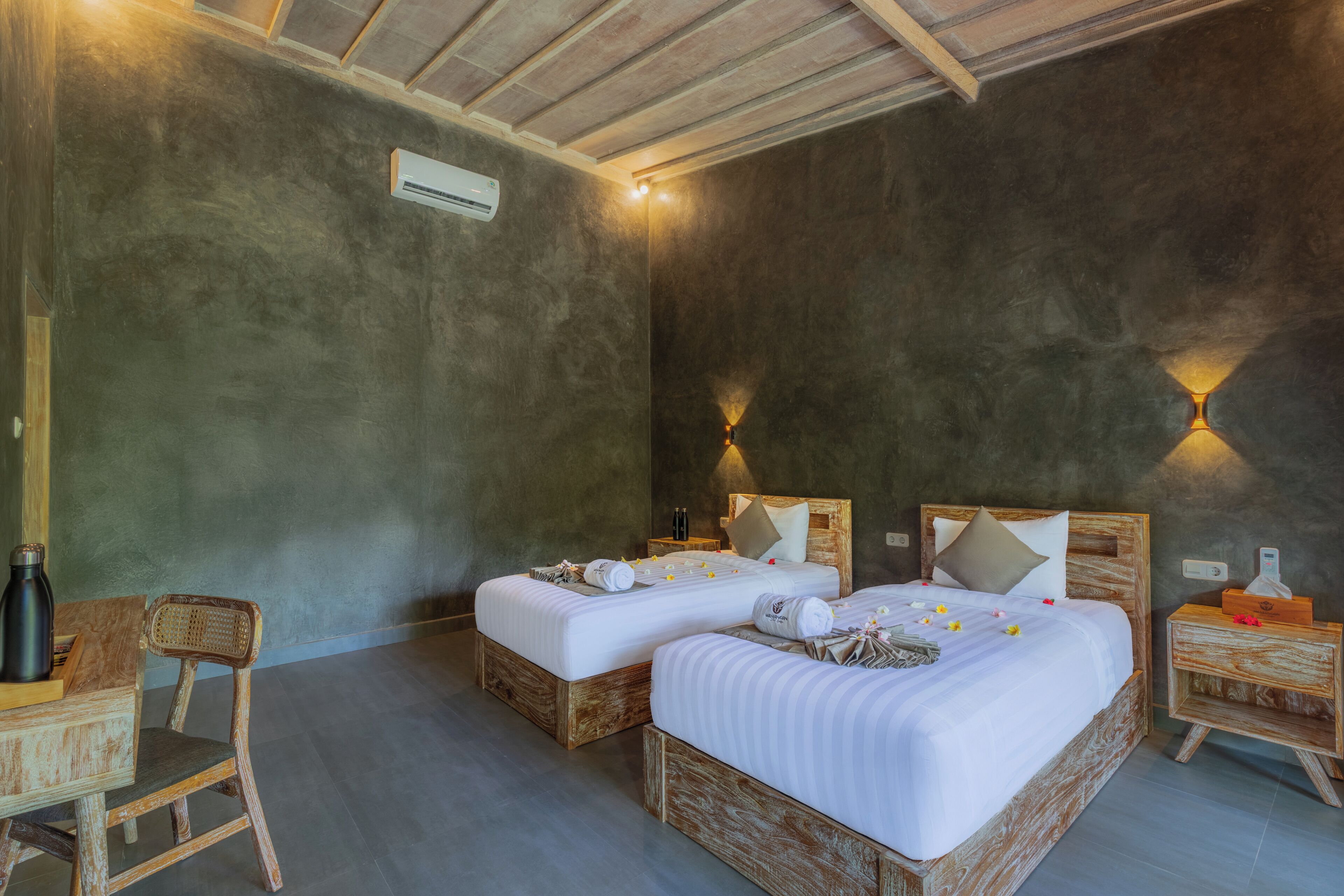Een kamer met twee bedden, een houten stoel, een nachtkastje en een wandairconditioner.
