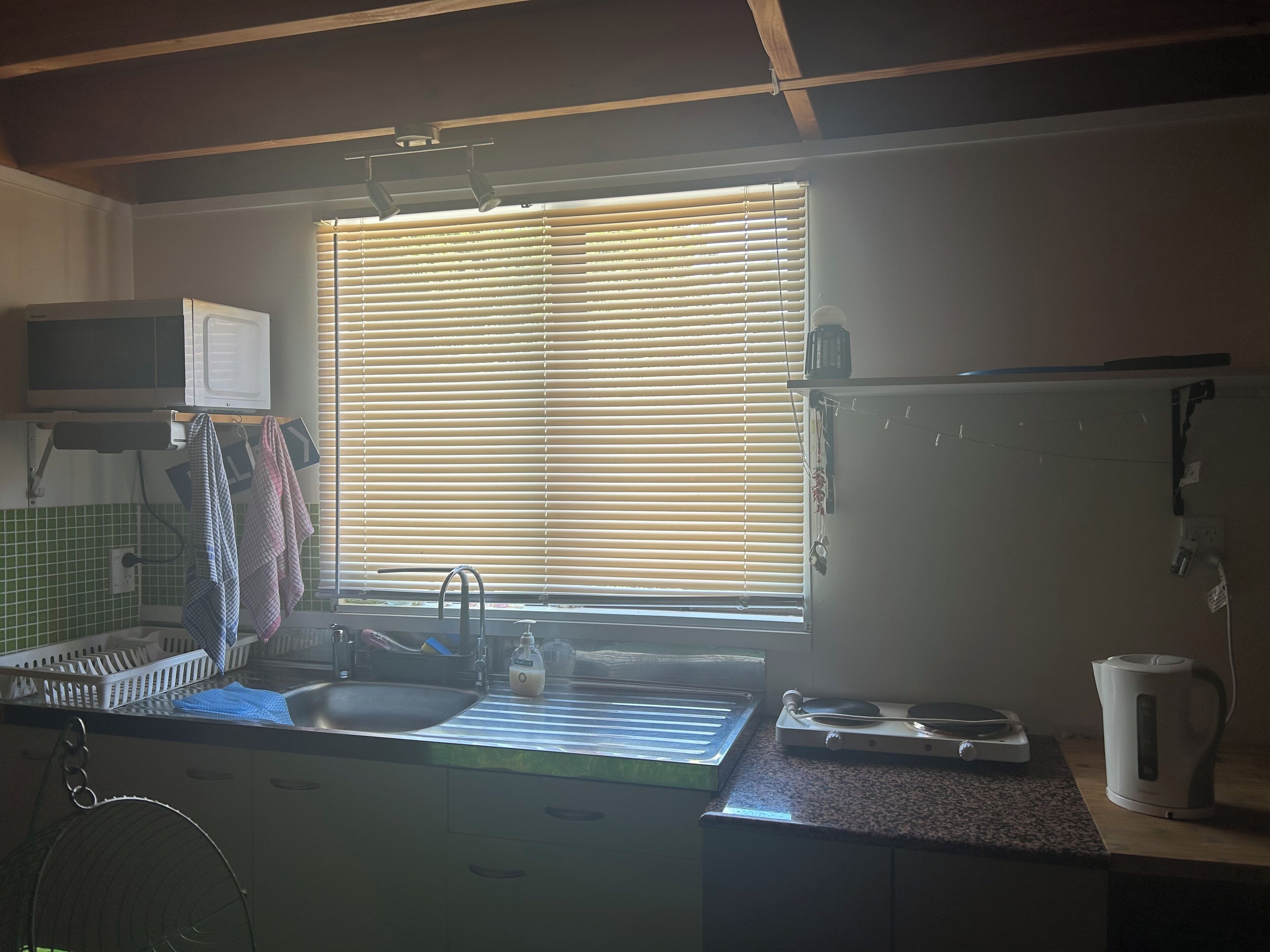 A kitchen with a window, sink, microwave, and kettle.