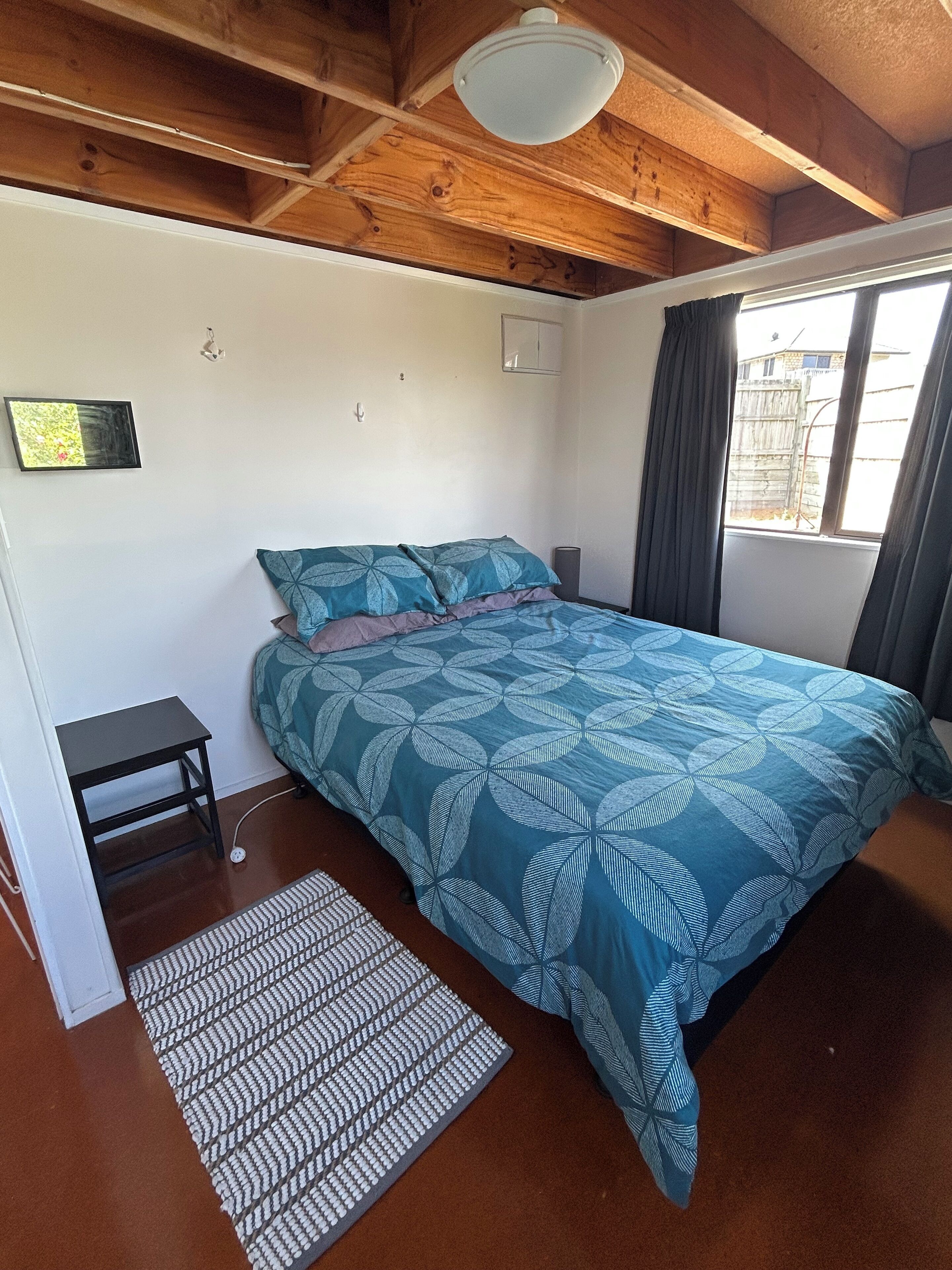 Un dormitorio con una cama, una mesita, una alfombra y una ventana con cortinas.