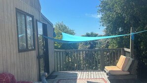 Eine Holzterrasse mit einem blauen Sonnensegel, einem roten, gemusterten Sofa und einem beigen Sofa mit Kissen.